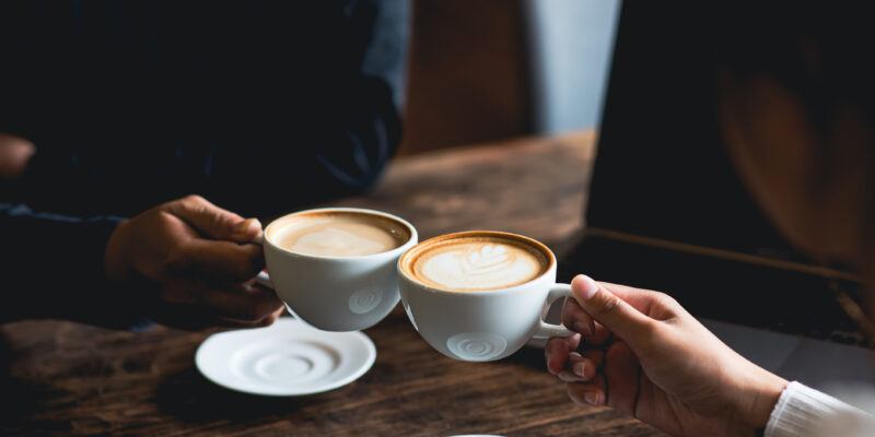 Close-up of a man and woman clinking a white coffee cup in a coffee shop. while talking at work
