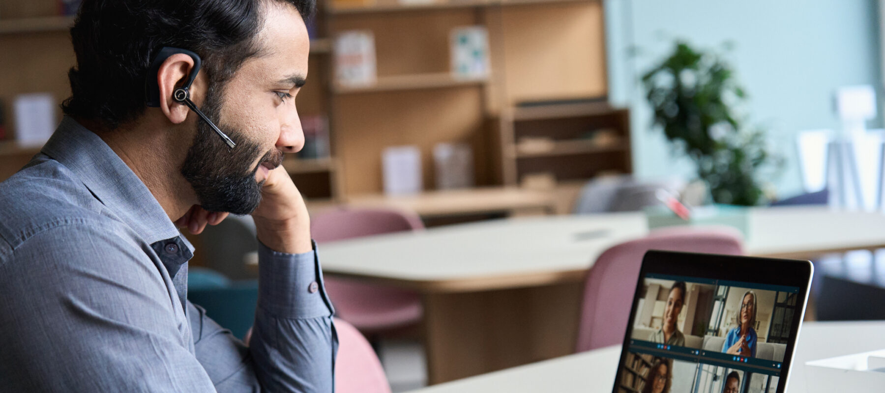 Indian business man wearing headset having virtual team meeting on video conference call using laptop work from home office talking to diverse people group in remote teamwork online distance chat.