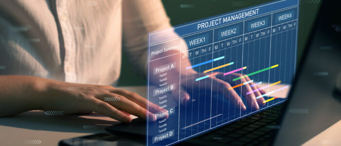 Project manager working on laptop and updating tasks and milestones progress planning with Gantt chart scheduling interface for company on virtual screen