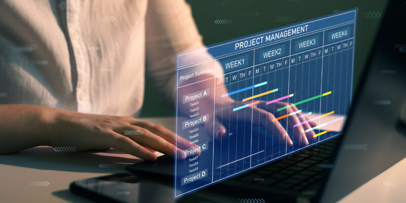 Project manager working on laptop and updating tasks and milestones progress planning with Gantt chart scheduling interface for company on virtual screen