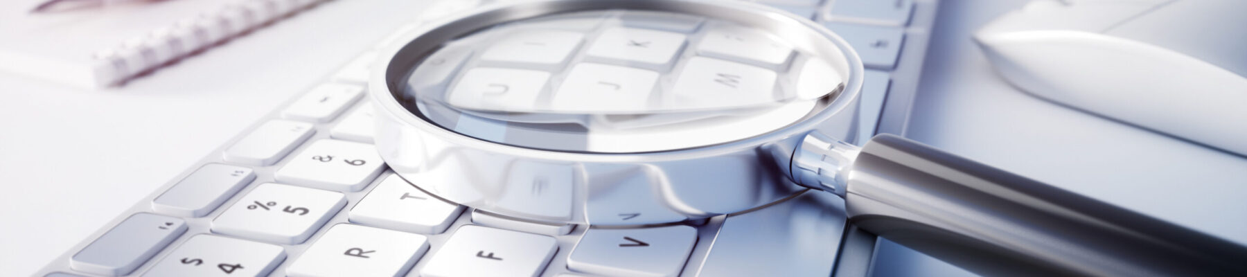 Magnifying Glass on white computer keyboard on white desktop with accessories.