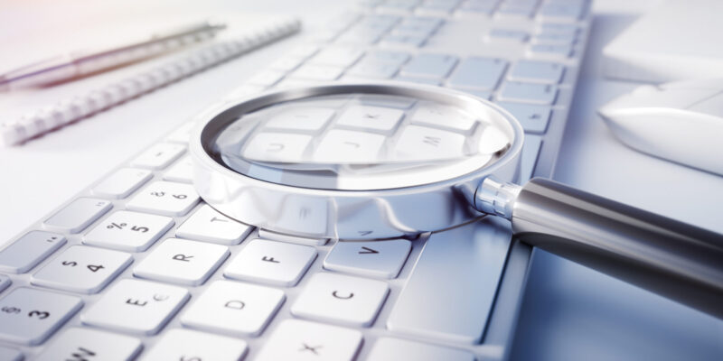 Magnifying Glass on white computer keyboard on white desktop with accessories.
