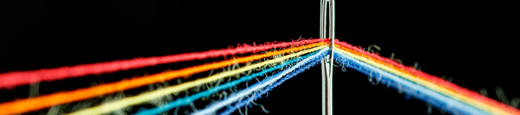 multi-colored threads for sewing in the form of a rainbow pass through an antique needle on a black background close-up