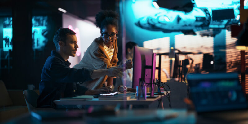 Portrait of Black Creative Director Giving Instructions on 3D Game Visuals to Male Developer in Creative Agency. Two Stylish Diverse Employees Discussing Design on Computer in Game Development Company